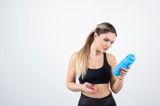 Blonde fit woman in black top standing and holding bottle of water with expander.  