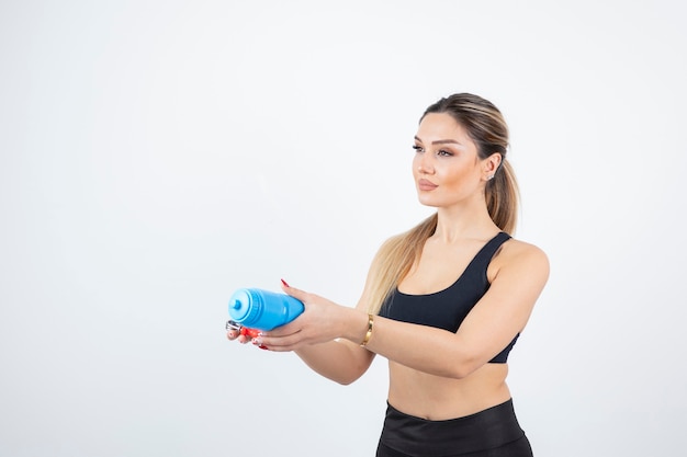 Blonde fit woman in black top standing and holding bottle of water with expander.  