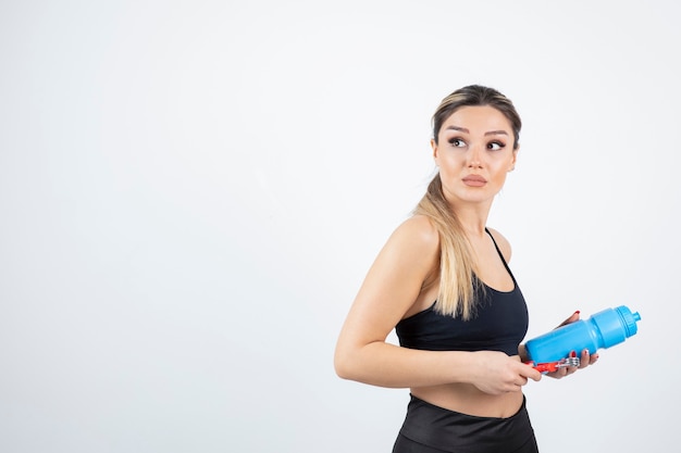 Blonde fit woman in black top standing and holding bottle of water with expander.  