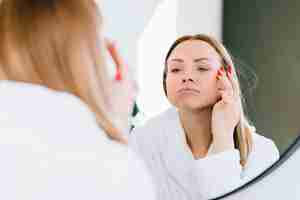 Free photo blonde girl applying cream on her face