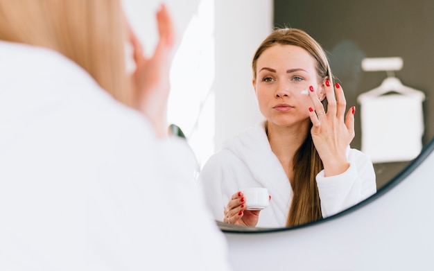 Free photo blonde girl applying cream on her face