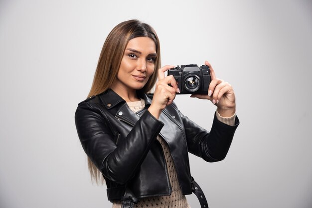 Blonde girl in black leather jacket taking her selfies with a camera.