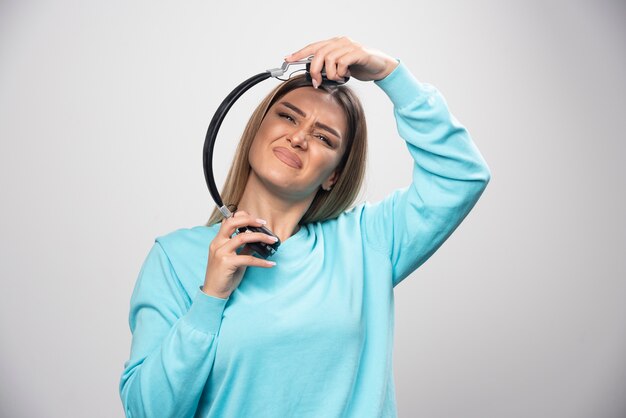 Blonde girl in blue sweatshirt listens the headphones and does not enjoy the music.