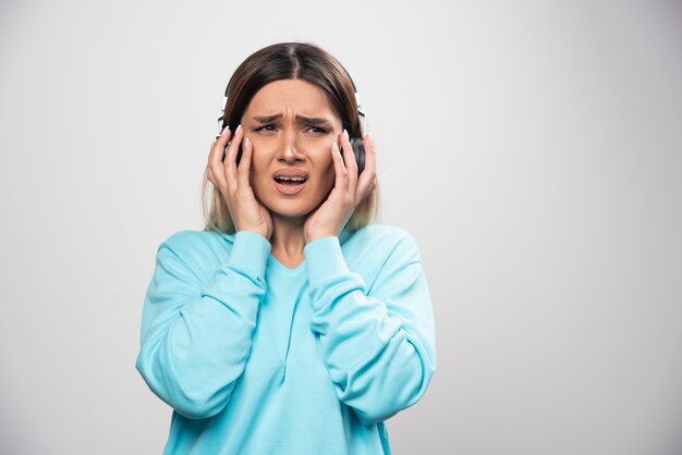 Blonde girl in blue sweatshirt listens the headphones and does not enjoy the music