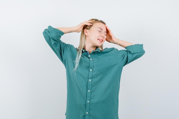 Blonde girl in green blouse putting hands on head, closing eyes and looking calm