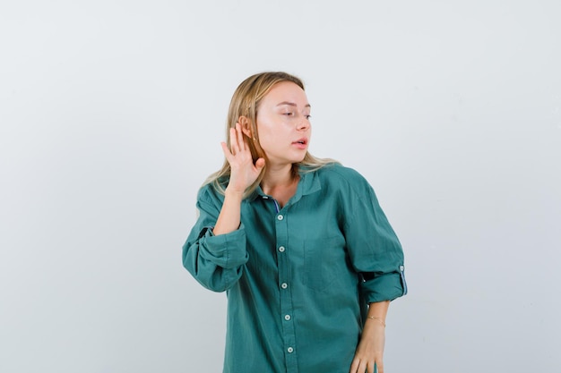 Free photo blonde girl holding hand near ear to hear something in green blouse and looking focused