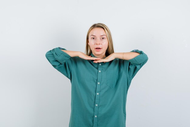 Blonde girl holding hands under chin in green blouse and looking pretty.