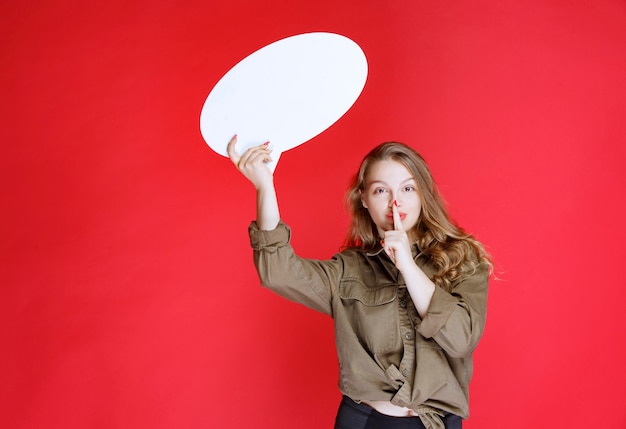 Free photo blonde girl holding an ovale thinkboard and asking for silence.