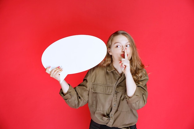 Free photo blonde girl holding an ovale thinkboard and asking for silence.