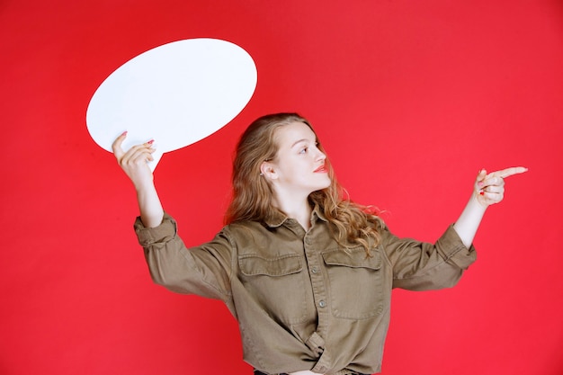 Free photo blonde girl holding an ovale thinkboard and pointing at it.