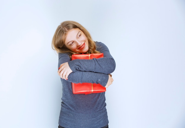 Free Photo blonde girl hugging her red gift box and feeling happy.