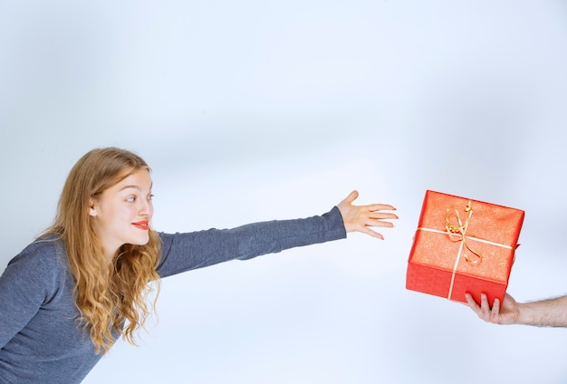 Free photo blonde girl is being offered a red gift box and she is longing ahead to take it.