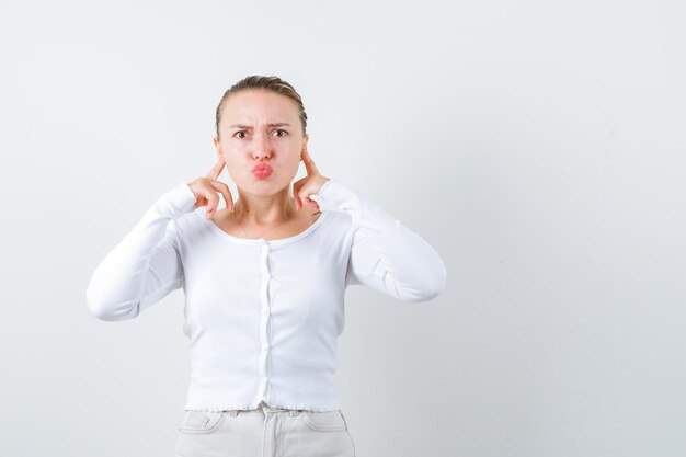 Blonde girl is closing her ears on white background