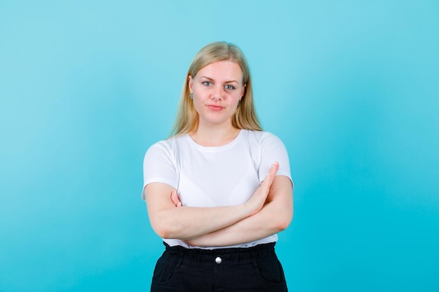 Free Photo blonde girl is looking at camera by crossing arms on blue background