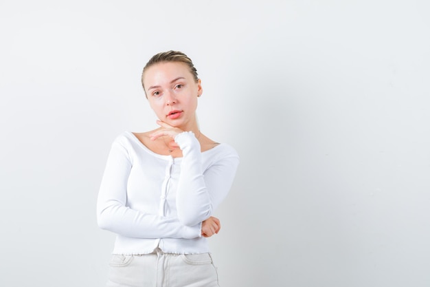 Blonde girl is putting her hand under her chin on white background