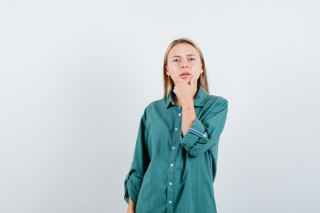 Free photo blonde girl leaning chin on hand in green blouse and looking pensive