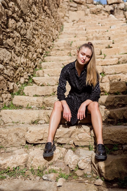 The blonde girl look at the left in black dress on stone background