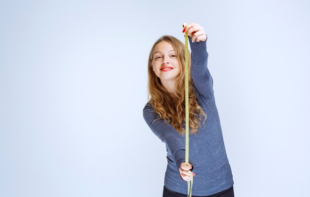 Free photo blonde girl opening the measuring tape and showing the result.