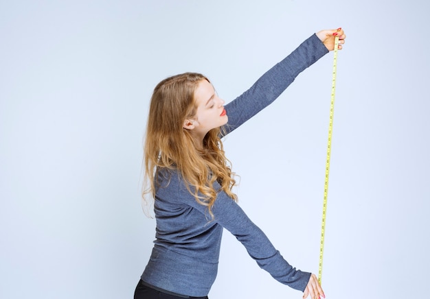 Free photo blonde girl opening the measuring tape and showing the result.