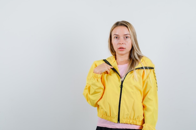 Free Photo blonde girl pointing at herself in yellow jacket and looking puzzled