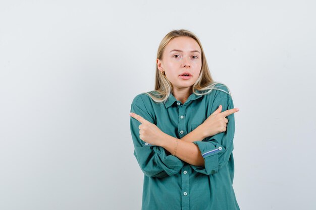 Blonde girl pointing opposite directions with index fingers in green blouse and looking radiant.