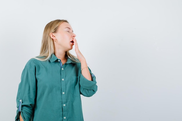 Free Photo blonde girl putting hand on mouth, yawning in green blouse and looking sleepy