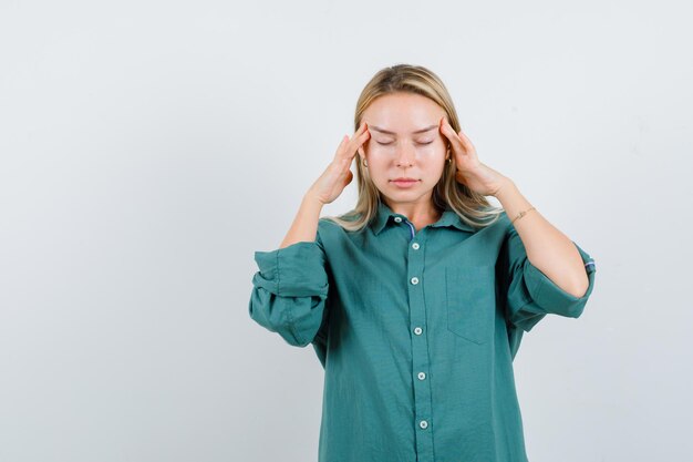 Blonde girl rubbing temples in green blouse and looking tired.