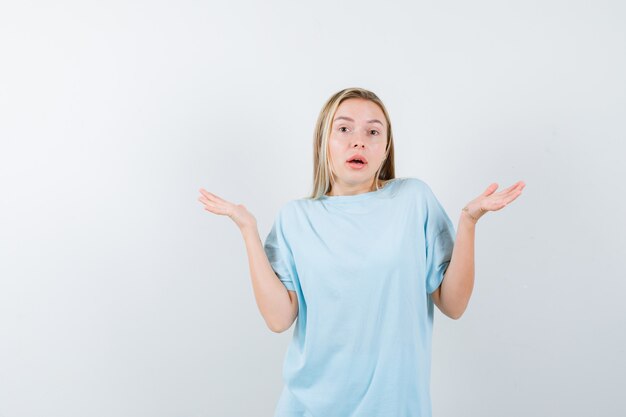 Blonde girl showing helpless gesture in blue t-shirt and looking confused. front view.