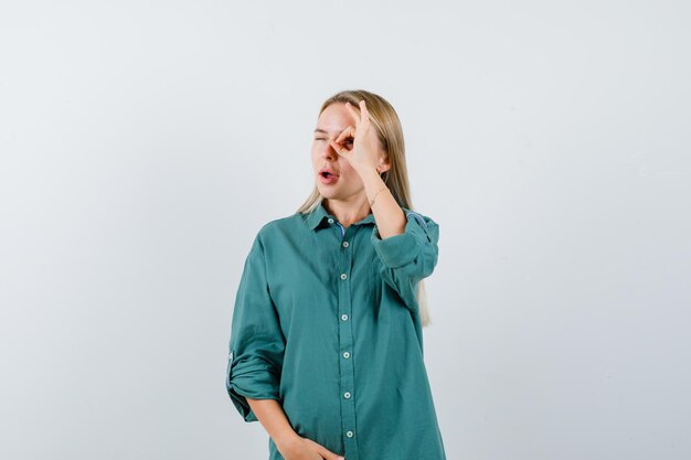 Blonde girl showing ok sign while holding hand on belly in green blouse and looking pretty.