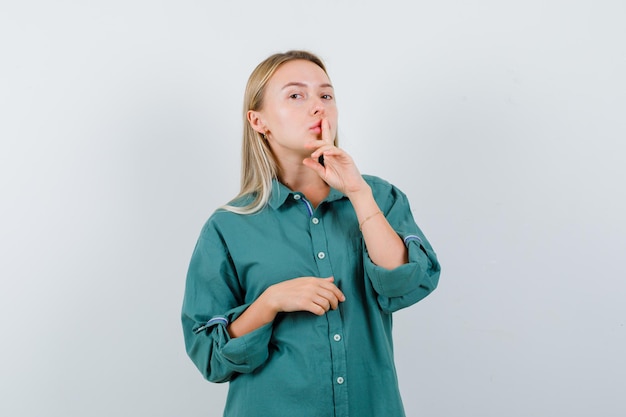 Free Photo blonde girl showing silence gesture in green blouse and looking radiant