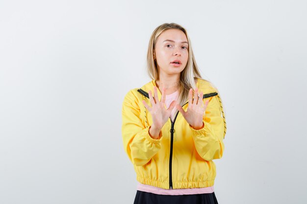 Free Photo blonde girl showing stop signs in pink t-shirt and yellow jacket and looking scared.