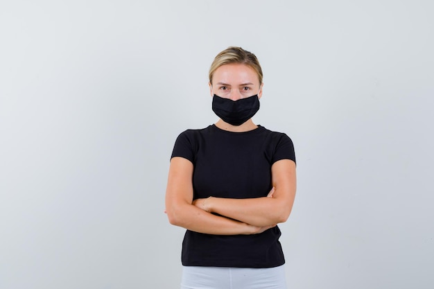 Blonde girl standing arms crossed in black t-shirt, white pants isolated