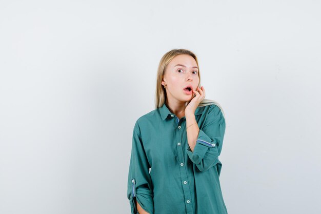 Blonde girl stretching one hand toward mouth in green blouse and looking pretty