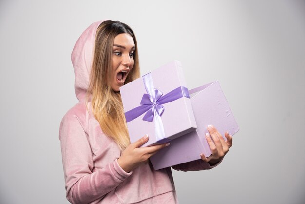 Blonde girl in sweatshirt received a gift box and feels positively surprized.