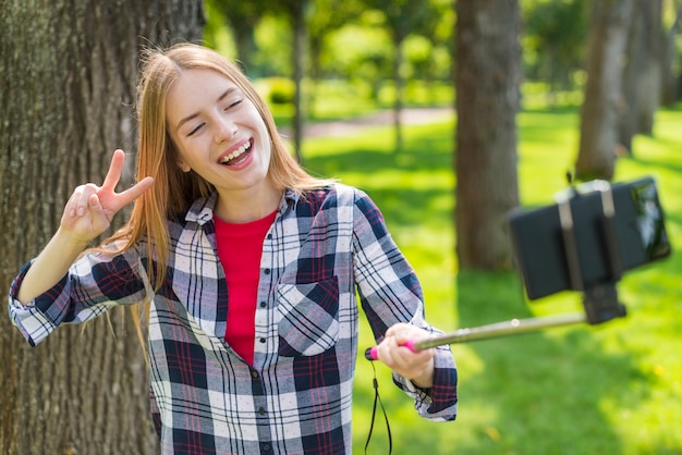 Blonde girl taking a selfie next to a tree