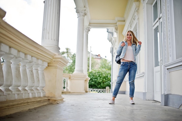 Blonde girl wear on jeans with backpack posed against vintage house