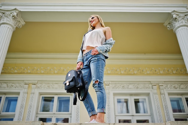 Free photo blonde girl wear on jeans with backpack posed against vintage house