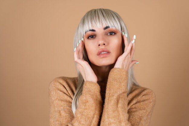 Blonde girl with bangs and brown daytime make-up in a sweater on beige background sensual fashion portrait