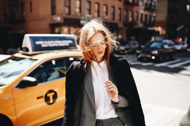 Free photo blonde lady in black coat stands on the sunny street somewhere in new york city