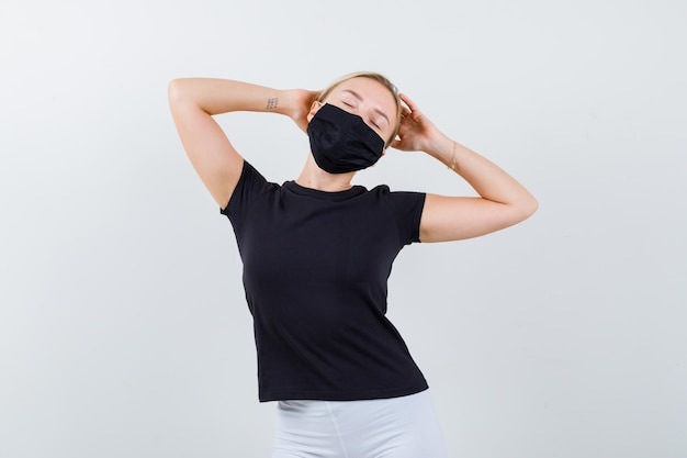 Free photo blonde lady in black t-shirt, black mask keeping hands behind head isolated