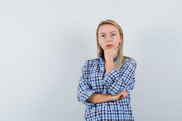 Blonde lady in casual shirt propping chin on hand and looking thoughtful