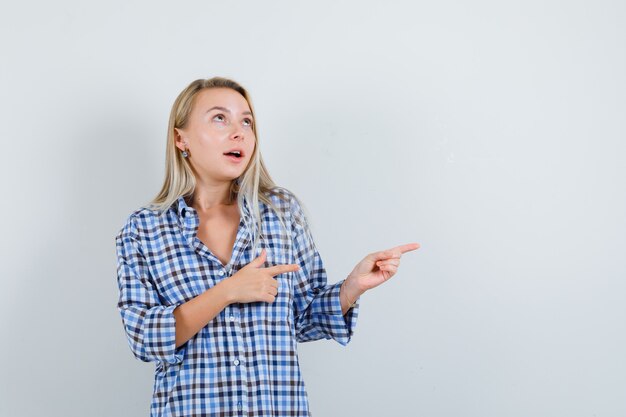 Blonde lady in checked shirt pointing to the right side and looking dreamy