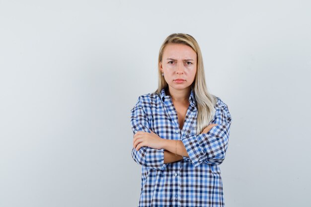 Blonde lady in checked shirt standing with crossed arms and looking offended