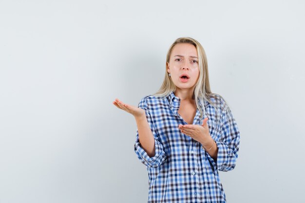 Blonde lady in checked shirt stretching hands in puzzled gesture