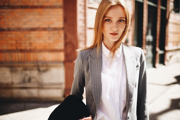 Free Photo blonde lady in grey suit enjoys the sunshine on the bright street of new york city