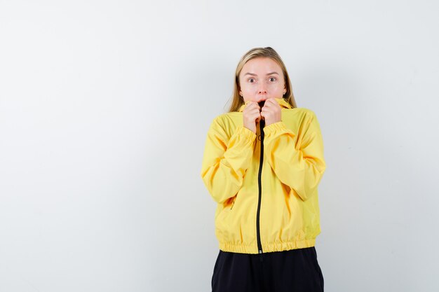 Blonde lady holding collar of her jacket in tracksuit and looking frightened. front view.