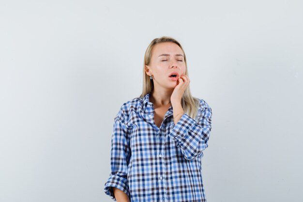 Blonde lady holding hand on chin in checked shirt and looking peaceful