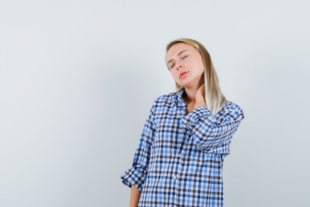 Free Photo blonde lady holding hand on neck in checked shirt and looking relaxed