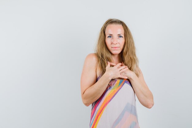 Blonde lady holding hands on chest in summer dress and looking grateful 