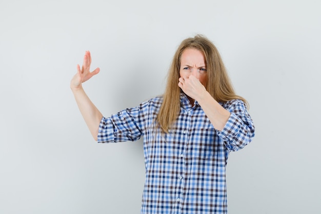 Blonde lady pinching nose due to bad smell in shirt and looking disgusted ,